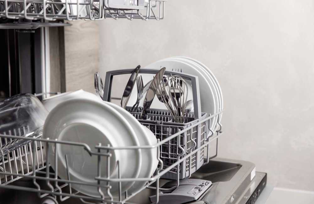 Hand placing white plates in a stainless steel dishwasher with an open door at Andrews Place in Panama City, Florida