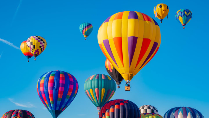 Many brightly colored hot air balloons ascend against a background of a clear blue sky | outdoor activities in Gilbert
