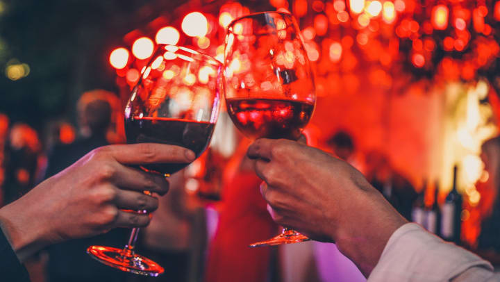 Two hands cheering with glasses of red wine on dinner date for two against a romantically lit background
