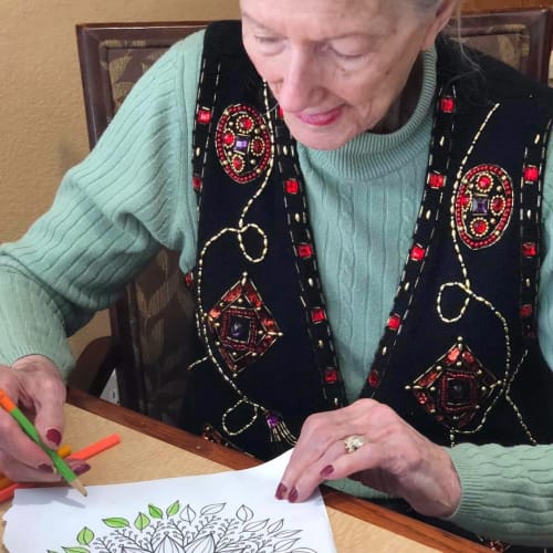 A smiling resident coloring a picture at Oxford Glen Memory Care at Sachse in Sachse, Texas