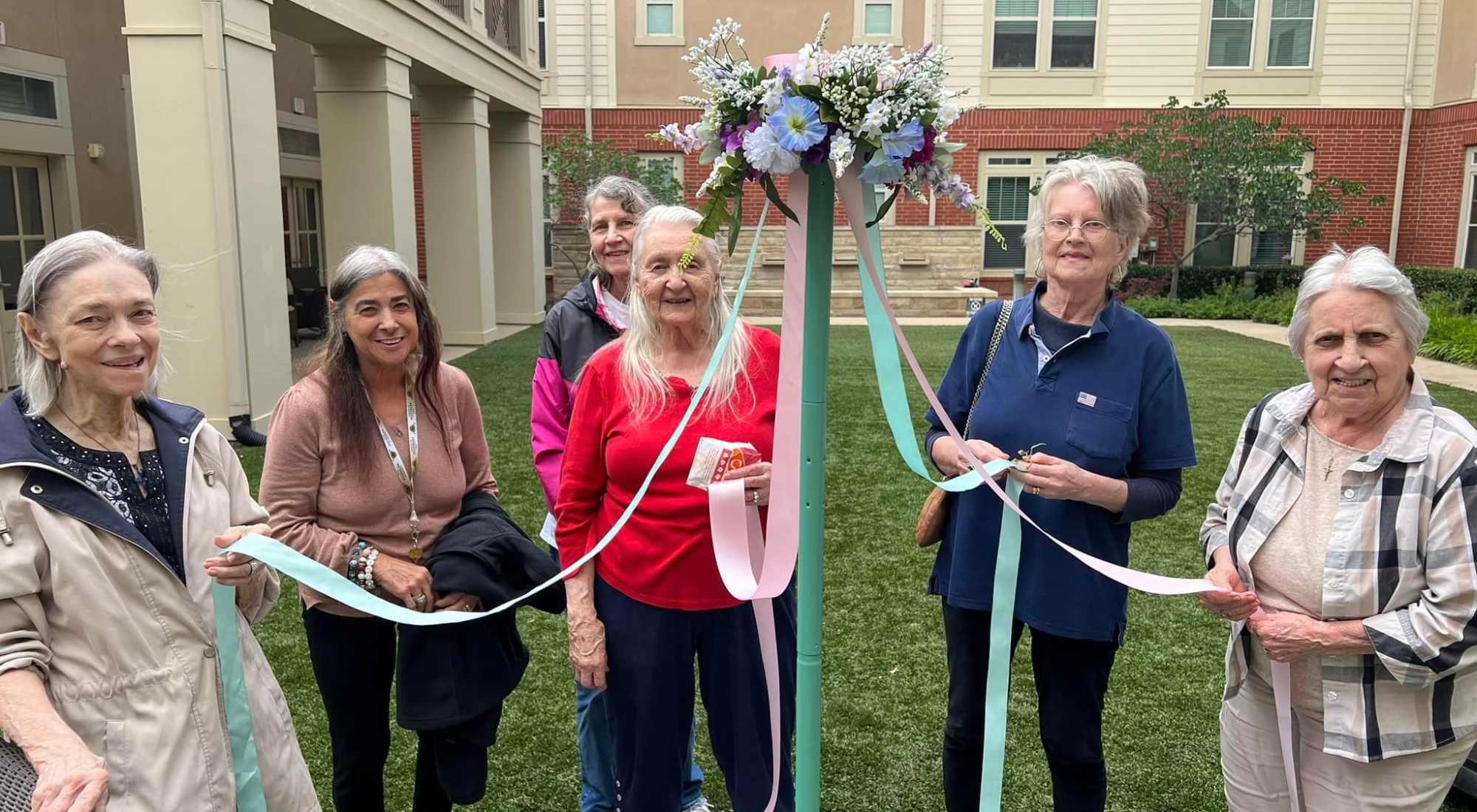 Elderly women celebrating spring outdoors with pastel ribbons at a maypole.