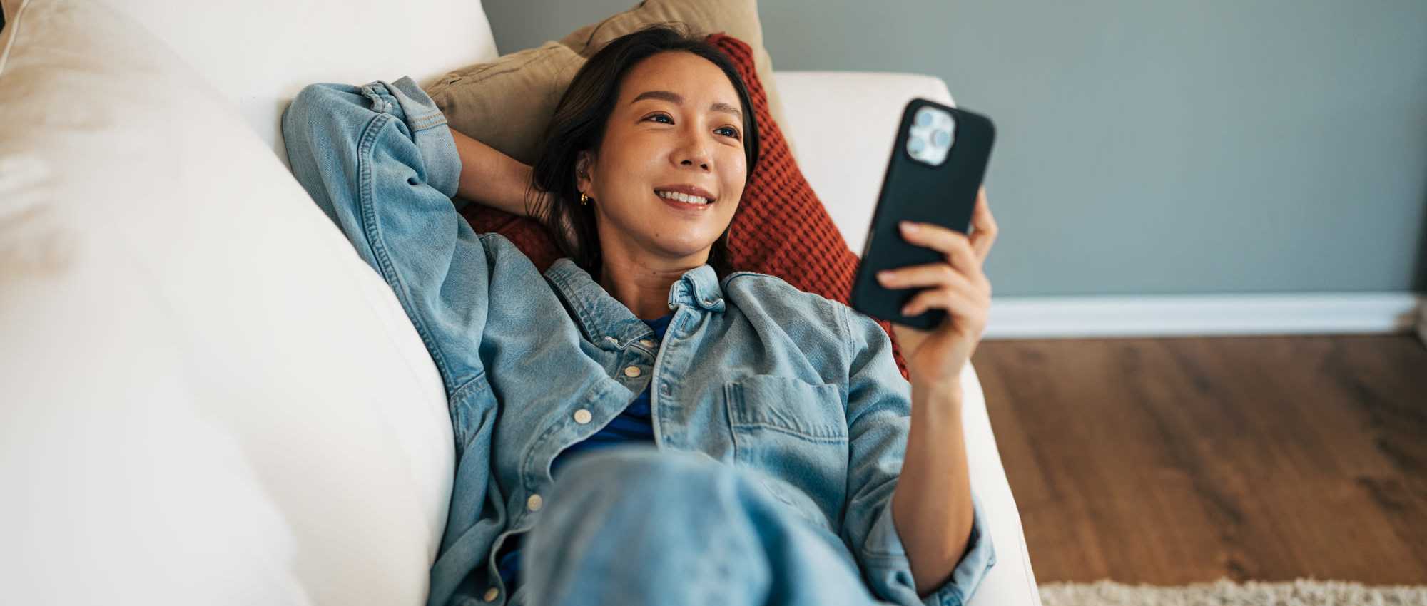 Woman relaxing on couch with smartphone at Villas at Mulberry Way in Kalamazoo, Michigan