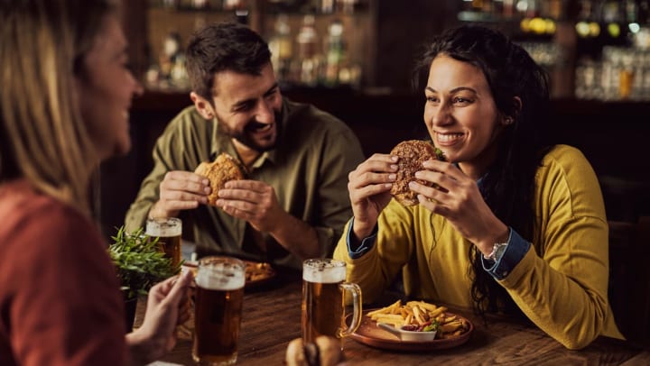 Two people eating burgers in a restaurant smiling in a conversation.