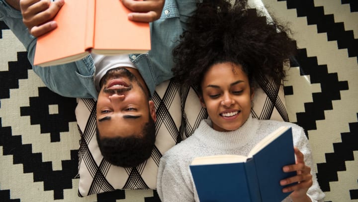 Two people lying on the floor holding books above their faces. 