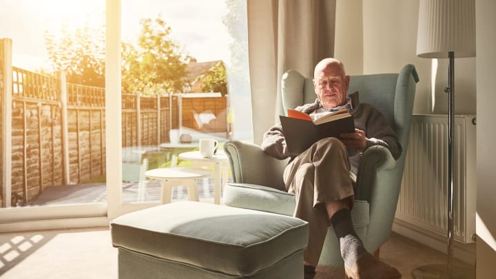 Older man sitting on an armchair reading a book.