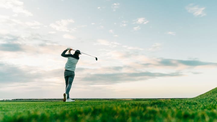 a lone golfer takes a swing with cloudy skies in the background