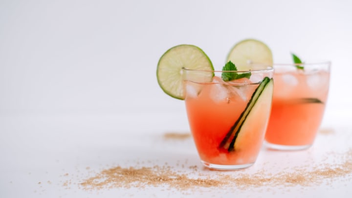 Grapefruit margarita with lime, mint, and ice against a white background.