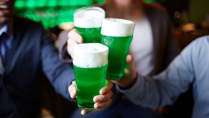 Three glasses of green beer held by group of men during a toast