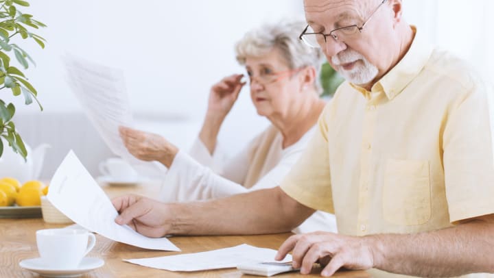 Couple sitting at desk sorting through papers working on Ways to fund senior living