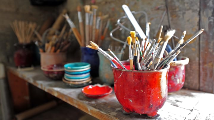 Six canisters on a shelf all filled with a variety of paint brushes | craft studios in Keller