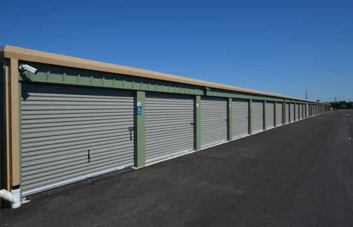 A row of clean drive up access storage facility doors. Green building with beige trim and gray doors. 