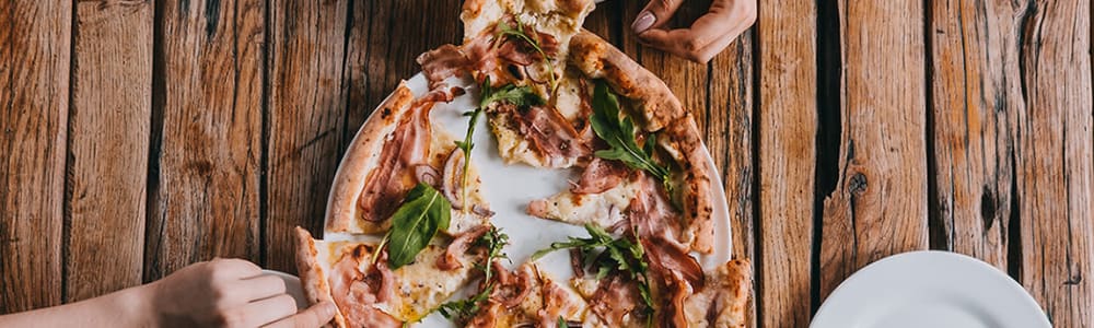 Hands grabbing pieces of a pizza at a restaurant near Walnut Creek Apartments in Macon, Georgia