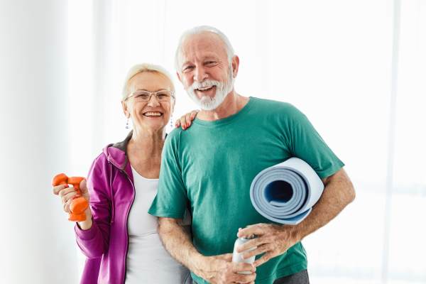 Senior couple smiling and holding yoga mats before a wellness class at The Reserve at Round Rock.