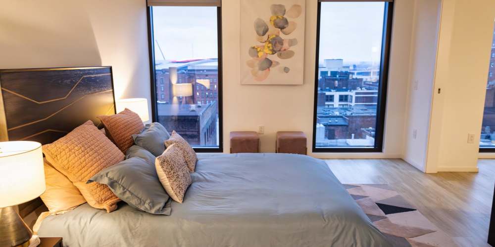A furnished bedroom with two widows viewing the surrounding city at The Beacon in Cleveland, Ohio