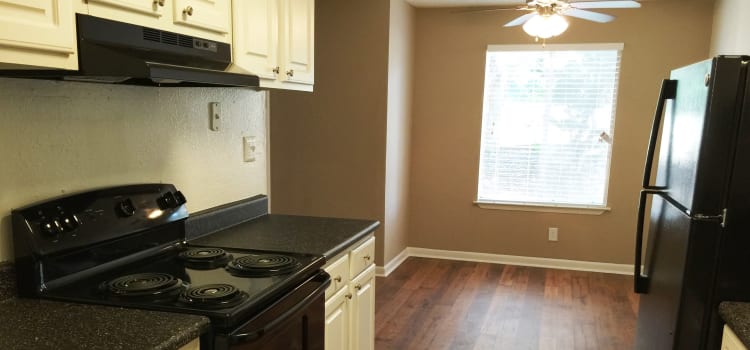 Ceiling fan, hardwood floors, and sleek black appliances in kitchen at Abbots Glen in Norcross