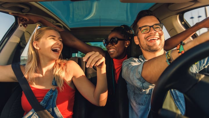 Three smiling friends enjoying traveling on a vacation in the car.