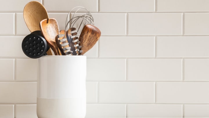 A stylish white subway tile backsplash with kitchen utensils in a ceramic jar on a granite countertop.