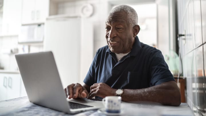 Elderly man looking at a laptop and smiling. 