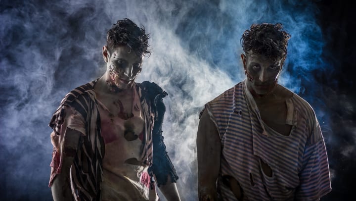 Two men dressed as zombies standing on black smoky background