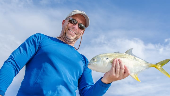 A smiling fisherman holds a fish in his hand, ready to be released.
