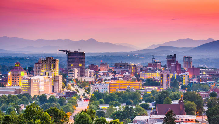 Asheville, North Carolina, skyline set against a mountainous backdrop at sunset.