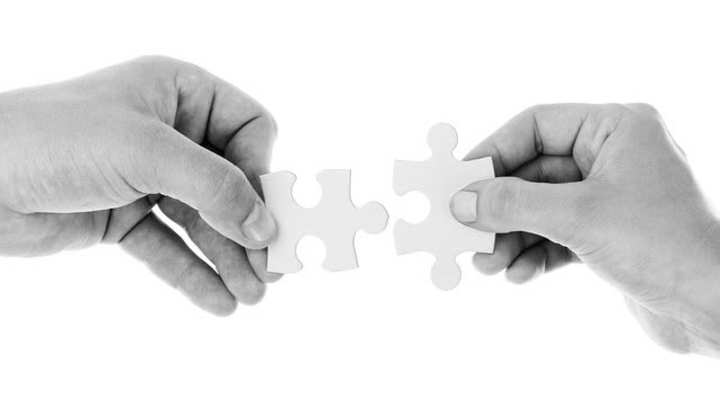 Two hands holding white puzzle pieces, bringing them together