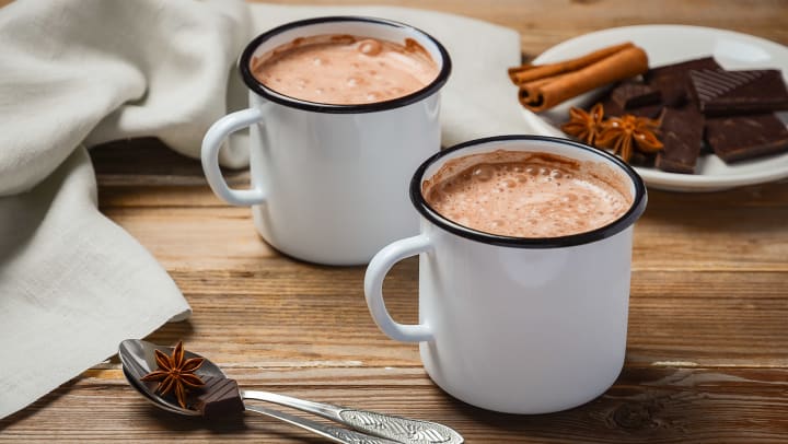 Two cups of hot chocolate on a rustic wooden table with chocolate pastries and cookies in the background