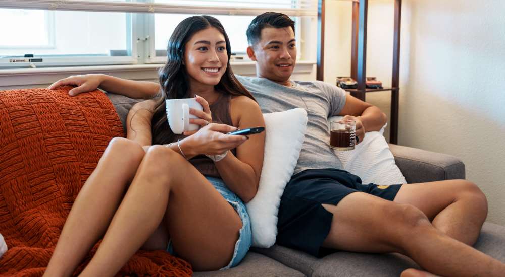 Happy residents watching TV while seating on a comfortable couch at Dawcrest Apartments in Olympia, Washington