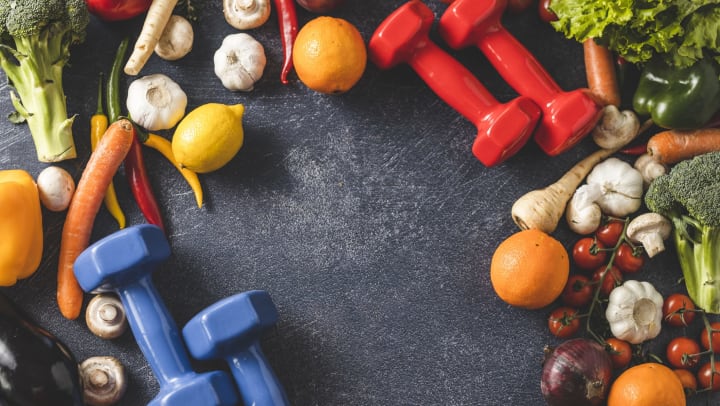 A colorful assortment of fruits and vegetables on a slate background with red and blue dumbbells