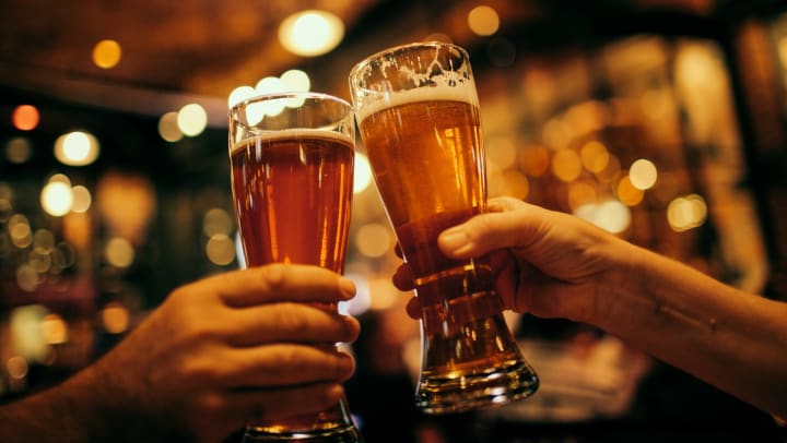 View inside a bar with two hands holding beer mugs and touching the mugs together
