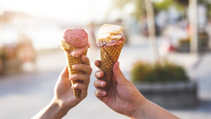 Two hands holding up multi-flavored ice cream cones with a sunlit backdrop