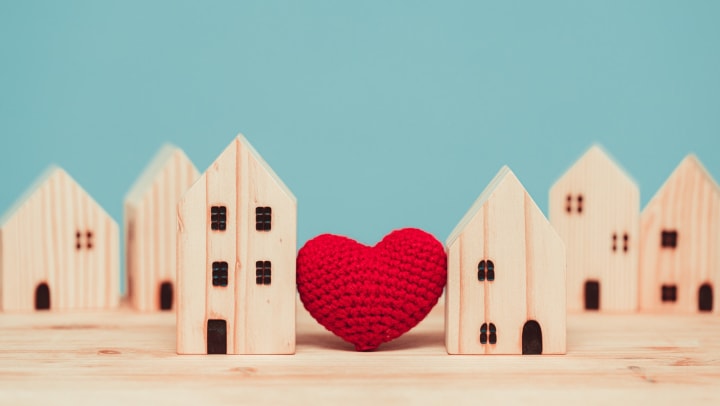 Knitted heart between wooden model homes, blue background.