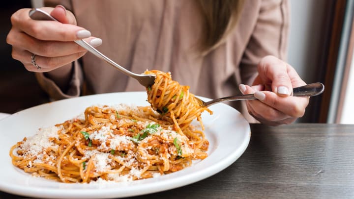 A woman twirls spaghetti around a fork while sitting at a restaurant table.