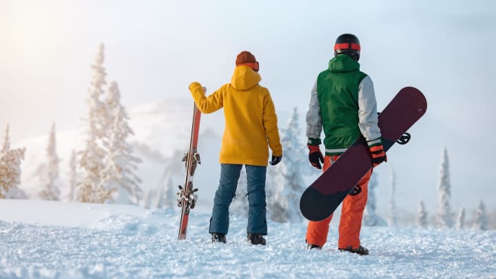Two people, one with a snowboard and the other with skis, standing in the snow.