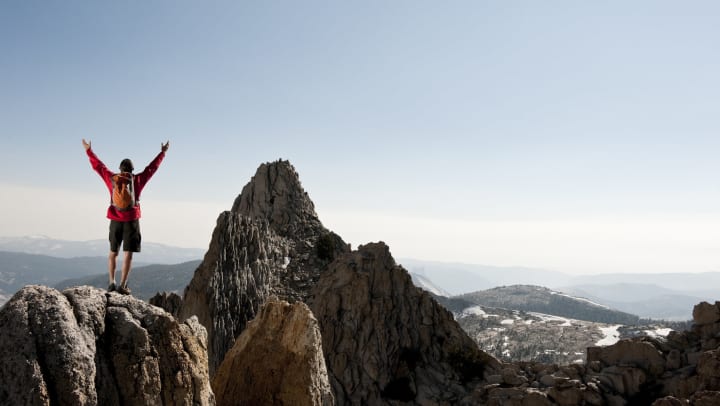 A person standing atop a rocky peak, arms raised in a V shape