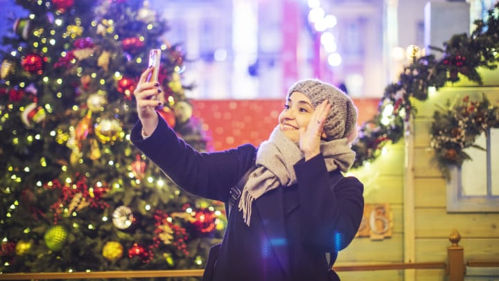 Smiling woman taking a selfie in front of a Christmas tree.