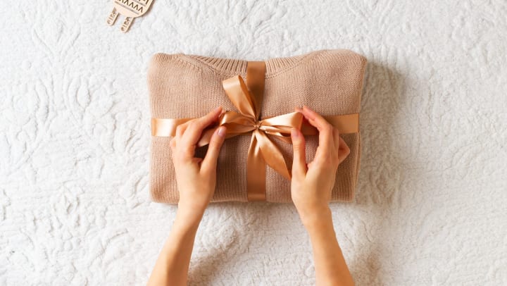 Hands giving wrapping a sweater with a ribbon bow on white blanket background