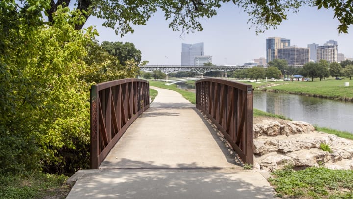 View of a trail bridge in Trinity Park with downtown Fort Worth in the background