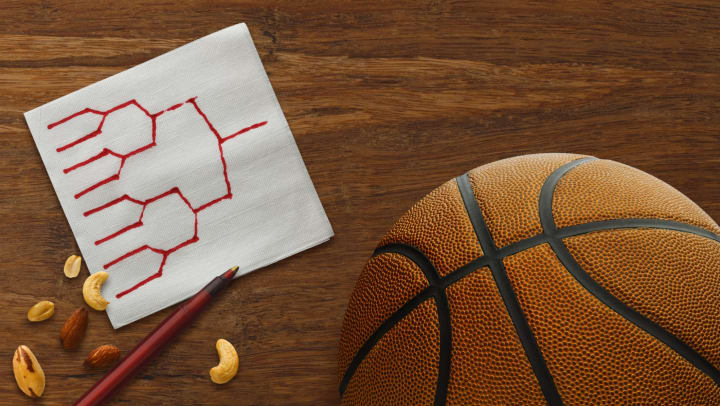 Basketball in corner with white paper bar cocktail napkin with playoff bracket drawn on it, next to some mixed nuts