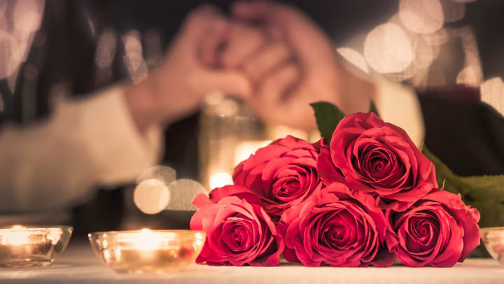 Roses and tealights in the foreground on a table, as a couple hold hands in the background.