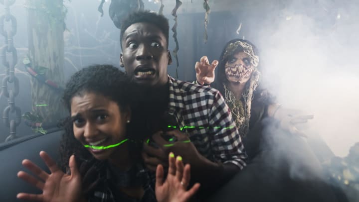 Two young adults having fun in a halloween haunted house being chased by a person in a scary costume. 