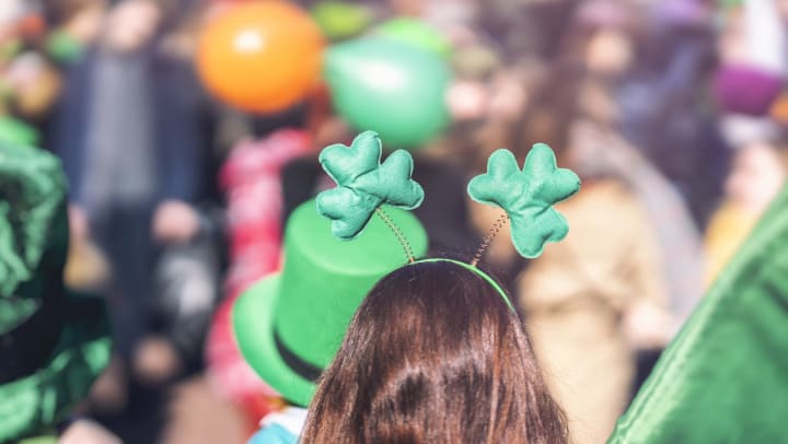 Back of heads with green hats and hair ornaments in foreground and celebration in background.