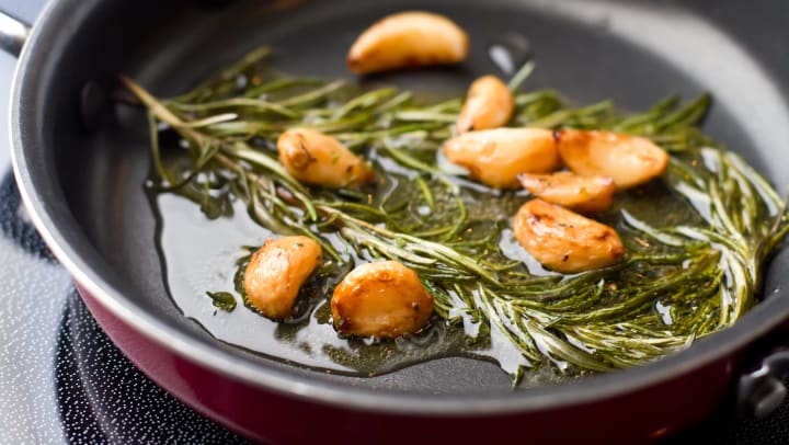 Close up shot of sauteed garlic and rosemary in olive oil in a pan.