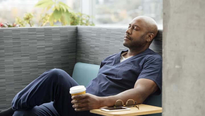 Man resting on a sofa with his eyes closed, holding a coffee cup