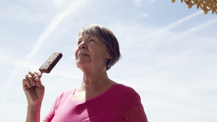 Senior woman standing outside in the sun holding an ice cream bar