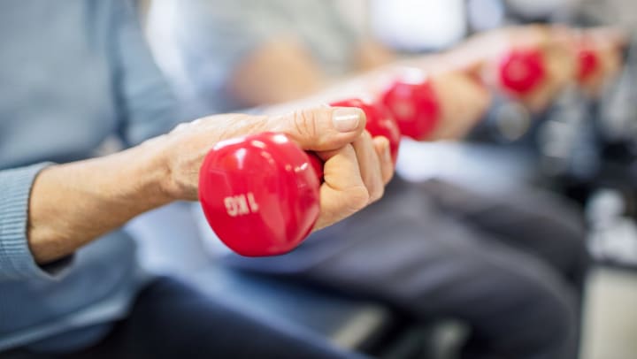 Close up of two women seated lifting up a pair of red dumbbell weights