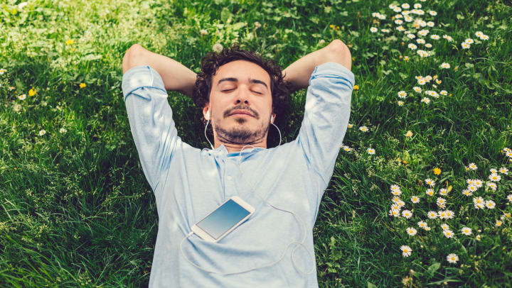 A man lying in the grass, with his eyes closed, listening to music on his headphones.