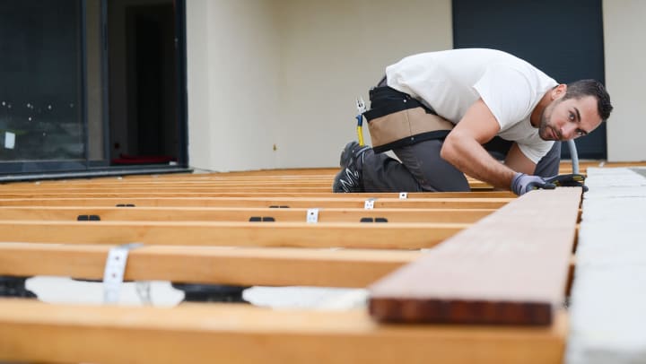 Man on his knees, working on a deck.