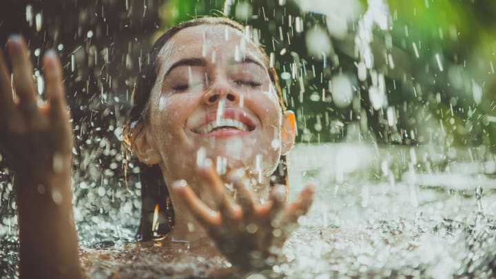 A smiling woman swimming under a waterfall 