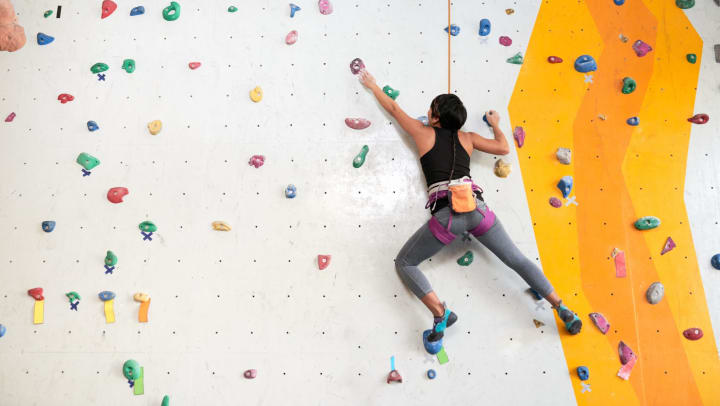 Woman climbing on the wall of an indoor rock climbing gym.